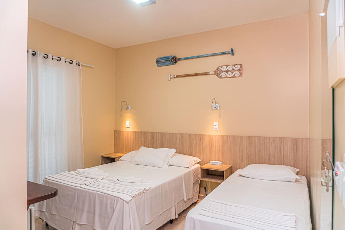 A hotel room with two beds, a wooden headboard, a wall-mounted paddle, and a curtain.