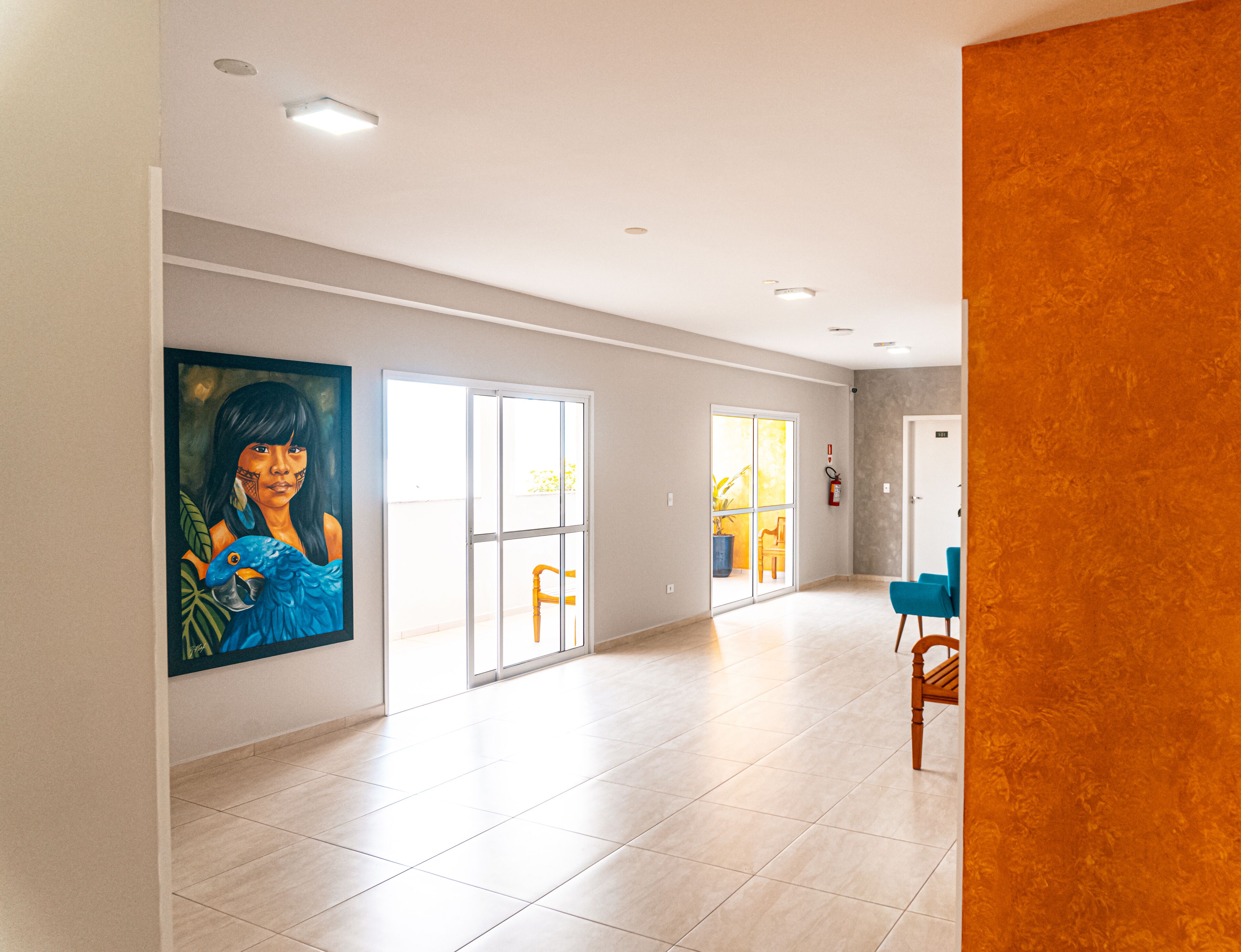 A spacious hallway with a large painting, a fire extinguisher, and a door with a view of the outside.