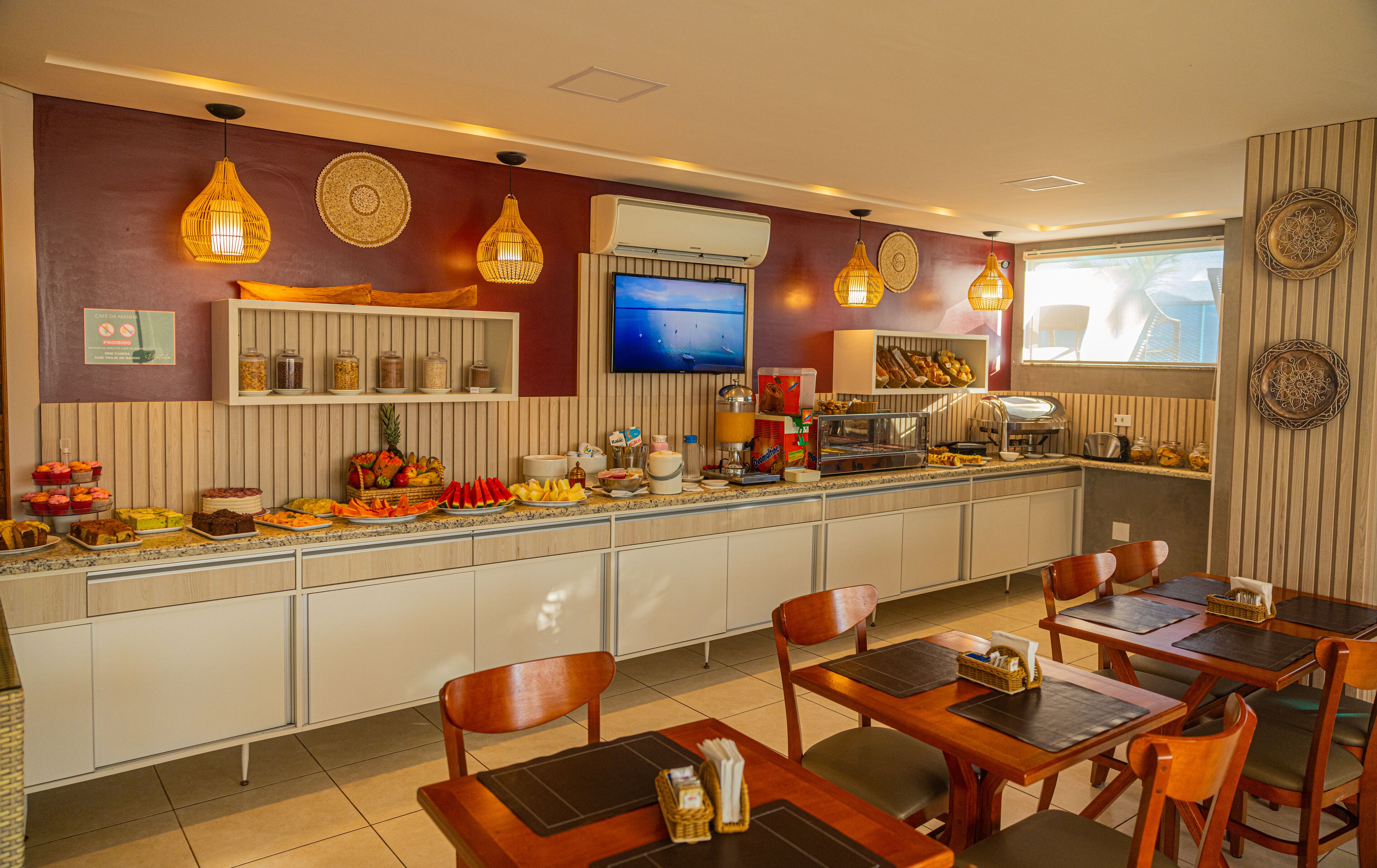 Una barra de desayuno con diversas opciones de comida, un televisor y un área de estar con mesas y sillas de madera.