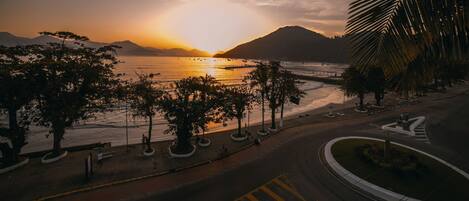 A coastal road with a sunset view, palm trees, and a distant mountain range.