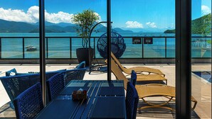 A terrace with wicker furniture, a potted plant, and a view of the sea and mountains. - Ubatuba Praia Hotel (Ubatuba)