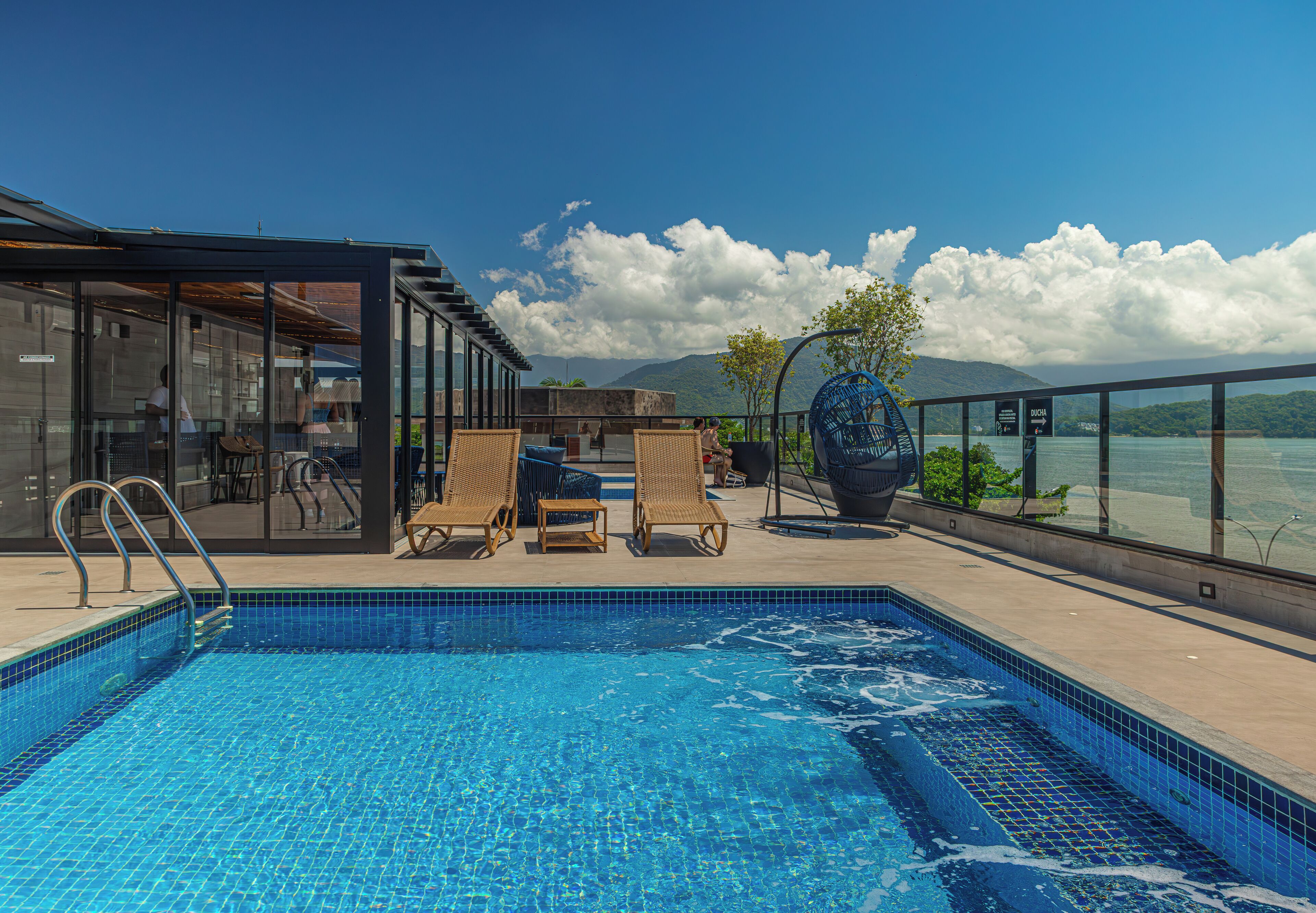 Piscina com espreguiçadeiras e área envidraçada com vista para a água.
