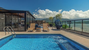 Piscina com espreguiçadeiras e área envidraçada com vista para a água.