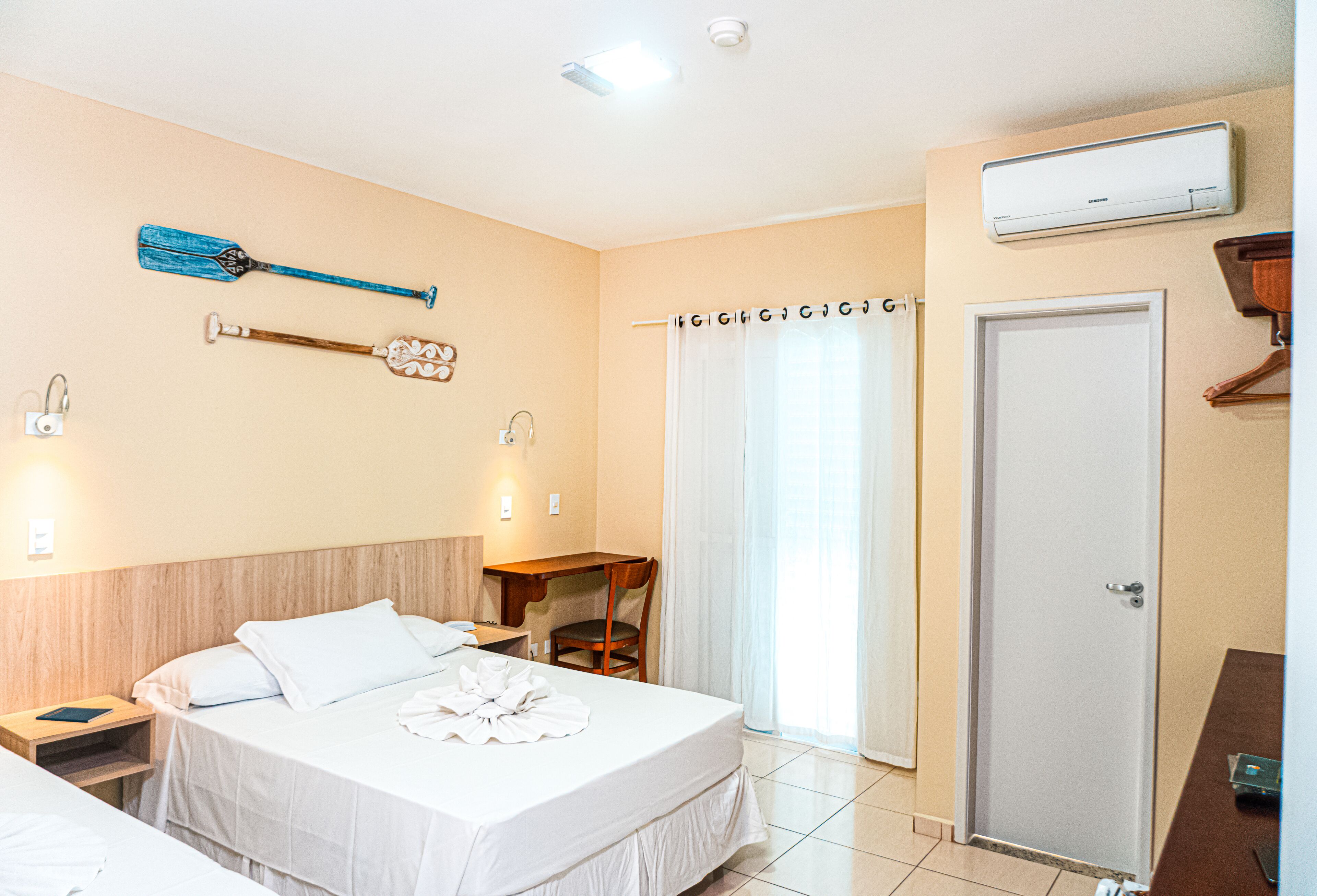 A hotel room with a bed, a desk, a chair, a wardrobe, and a bathroom with a shower curtain.