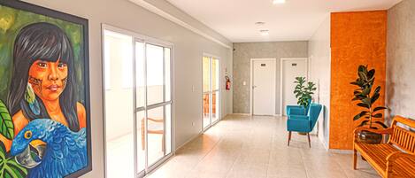 Un pasillo con un cuadro grande, una silla azul, un banco de madera y una planta en maceta.