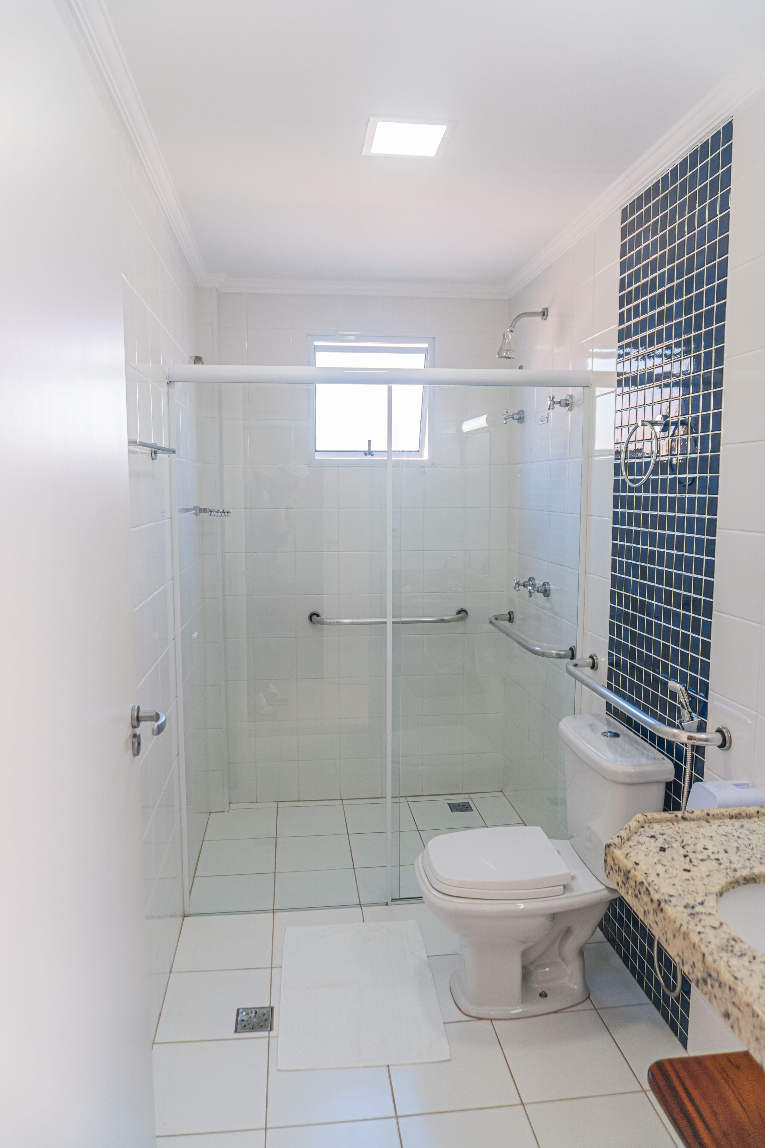 Ein modernes Badezimmer mit einer gläsernen Duschkabine, einer Toilette und einem Waschbecken mit Granitplatte.