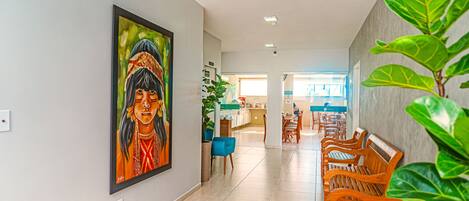 A hallway with a painting, wooden benches, and potted plants.