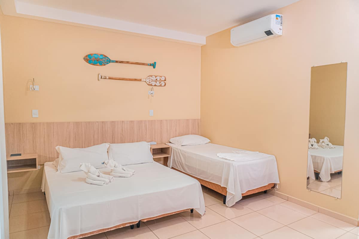 A hotel room with two beds, a wooden headboard, a wall-mounted air conditioner, and a mirror reflecting the room.