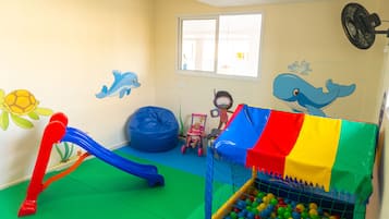 Zona de juegos con tobogán, piscina de pelotas y decoraciones de pared coloridas.