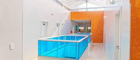 A modern hotel lobby with a glass ceiling, a central reception area, and a corridor leading to rooms.