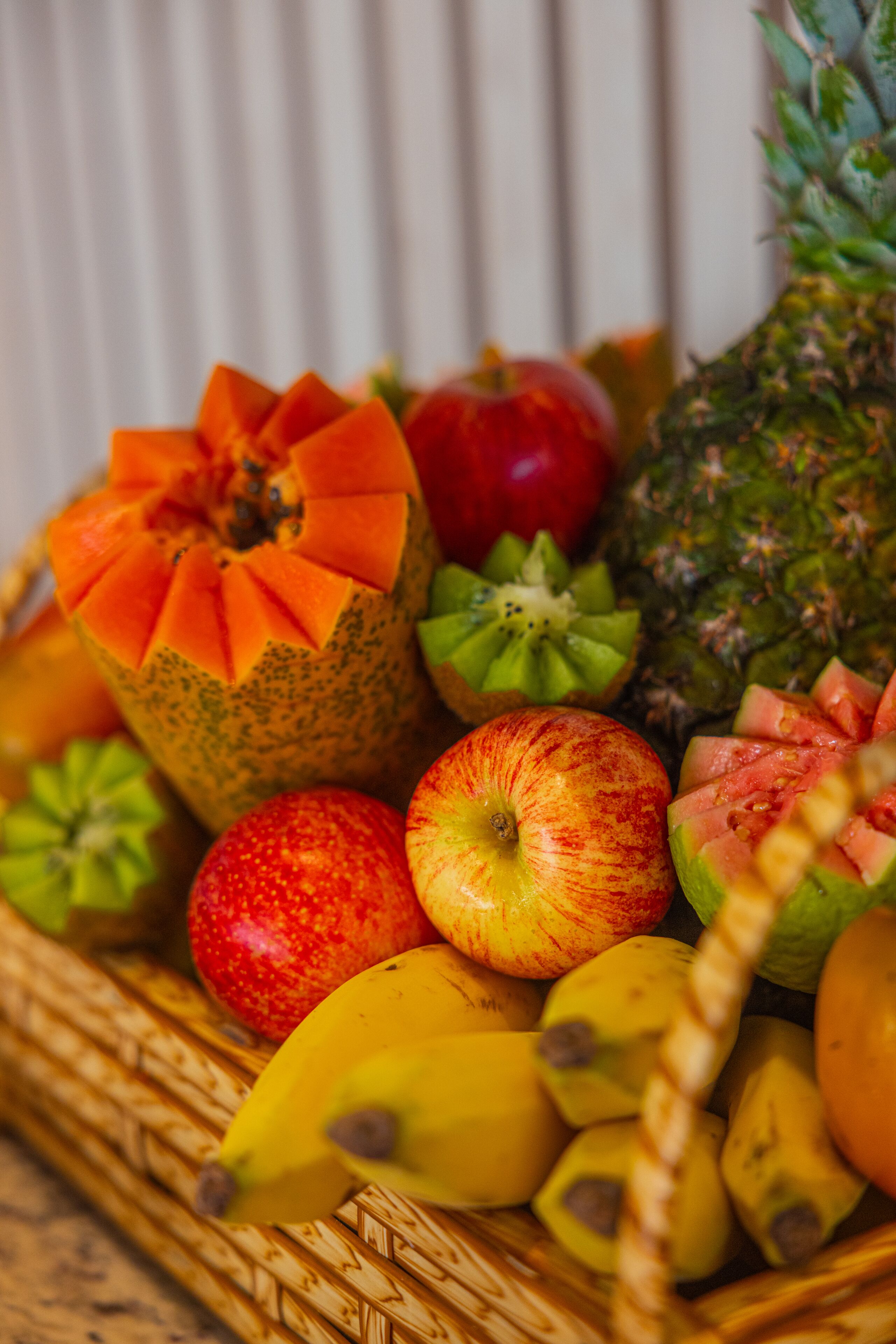 A basket of fruits including papaya, pineapple, apple, and banana.