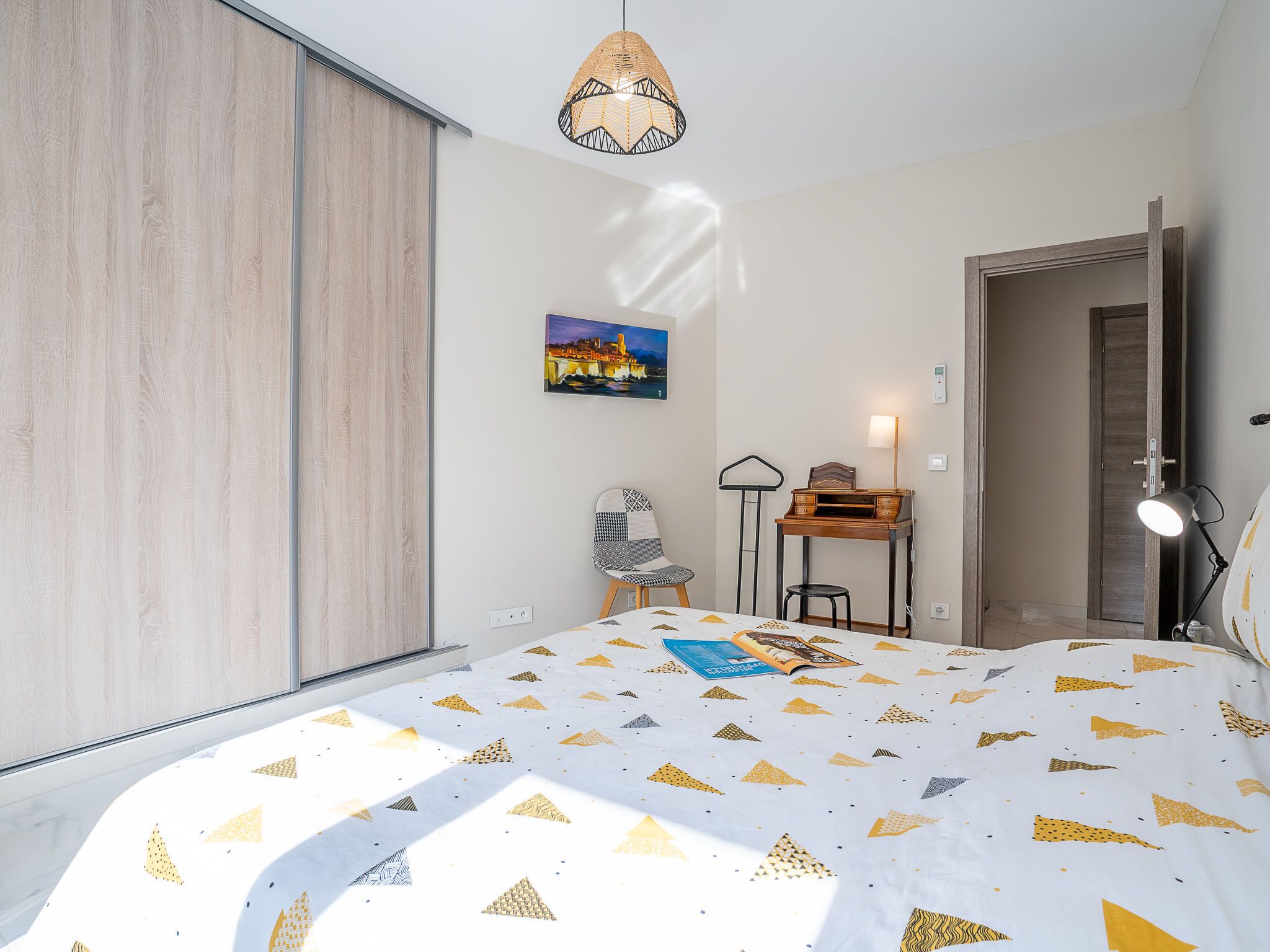 Une chambre à coucher comprenant un lit, un bureau, une chaise, un luminaire suspendu et un tableau accroché au mur.
