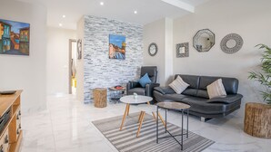 Un salon moderne avec un mur en pierre, un canapé en cuir noir, une table basse ronde et une table d’appoint en bois.