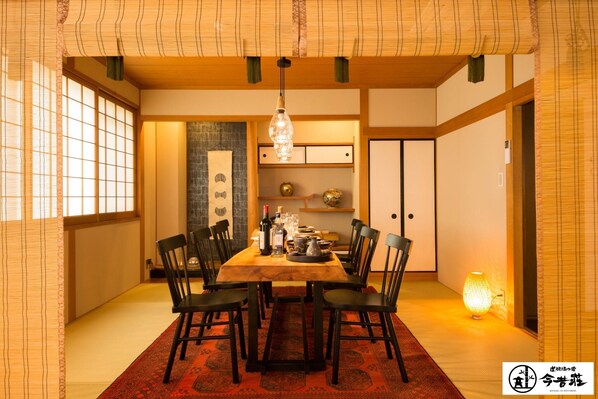 Une salle à manger japonaise traditionnelle avec un sol recouvert de tatamis, une table basse en bois, des chaises noires et un luminaire suspendu.