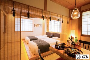 Une pièce de style japonais traditionnel, avec deux lits, une table en bois sur laquelle sont posées des bouteilles, et un luminaire suspendu.