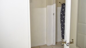 Een smalle gang met een witte deur aan de rechterkant, een witte muur en een betegelde vloer.