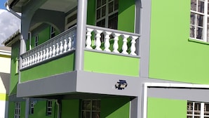Een gebouw met twee verdiepingen, een groene gevel, witte raamkozijnen en een balkon met witte hekwerk.