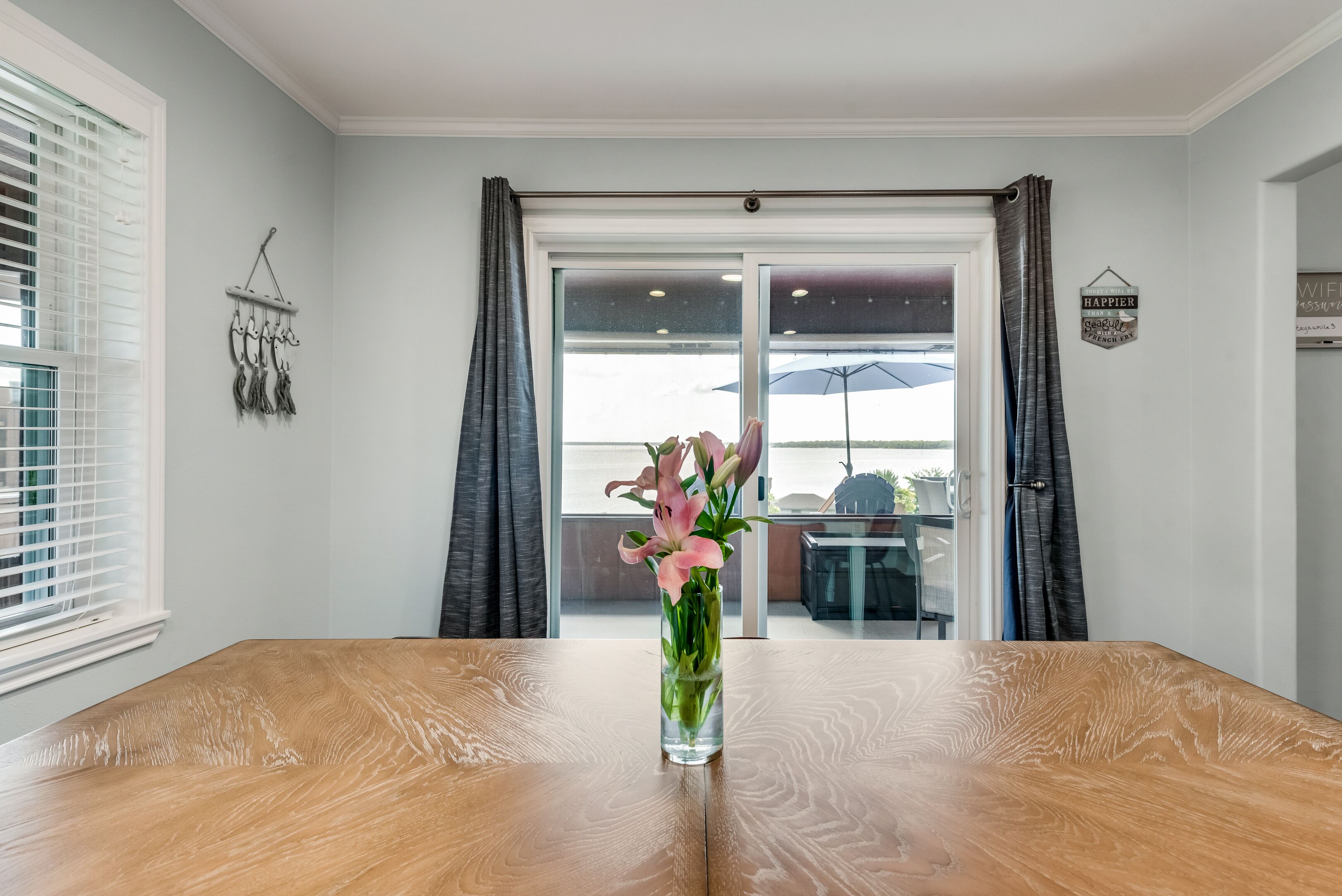 A dining area with a wooden table, a vase with flowers, and a view through a glass door to an outdoor seating area.
