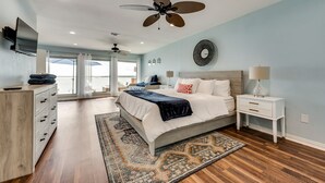 A spacious bedroom with a large bed, a ceiling fan, a TV, and a view of the outdoors.