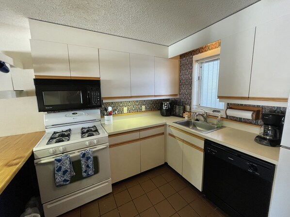 A compact kitchen with white cabinets, a microwave, stove, sink, and dishwasher.