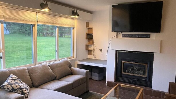 A living room with a sofa, a glass coffee table, a fireplace, and a TV mounted above it. - Private 2Bd 2Bath - Sleeps 5/6 Town home In Stowe VT - 15min From The Mountain (Stowe)