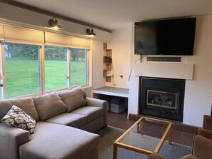 Una sala de estar con sofá, una mesa de centro de vidrio, chimenea y televisor montado en la pared.