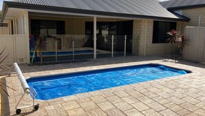 A residential backyard with a swimming pool, a covered patio area, and a fenced yard. - Central 3 Bed home with pool, EV Charger and unlimited free Wi-Fi (Busselton)