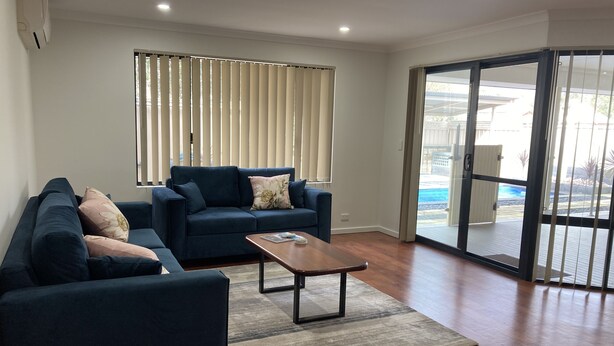A living room with a dark blue sofa set, a coffee table, and a large window with blinds. - Central 3 Bed home with pool, EV Charger and unlimited free Wi-Fi (Busselton)