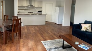 A modern kitchen with white cabinets, a central island, and a dining area with wooden chairs and a table. - Central 3 Bed home with pool, EV Charger and unlimited free Wi-Fi (Busselton)