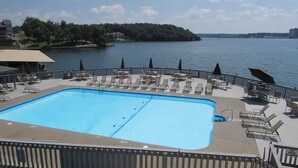 Ein rechteckiger Pool mit Liegestühlen und Sonnenschirmen auf einer Terrasse mit Blick auf einen See.