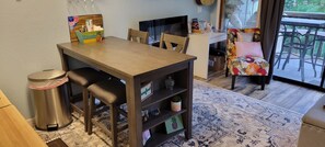 Un coin repas comprenant une table en bois, des chaises, une poubelle et une bibliothèque.