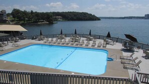 A rectangular pool with lounge chairs and umbrellas on a deck overlooking a lake. - LAKEFRONT CONDO READY FOR SUMMER FUN! DON'T DELAY! BOOKS UP EVERY SUMMER! (Lake Ozark)