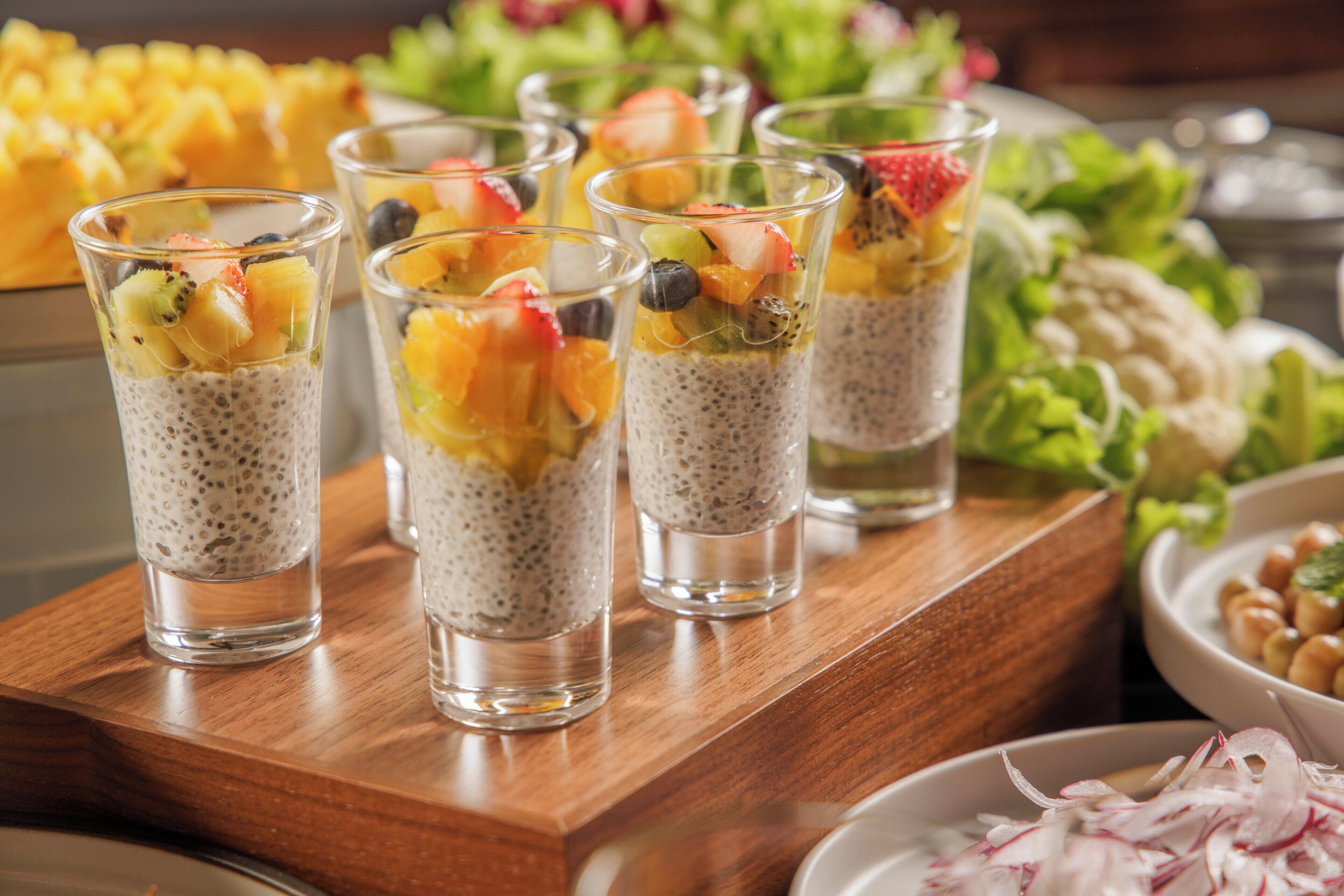 A wooden table with several glasses containing chia seed pudding topped with fruits.