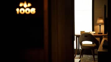 Een hotelkamer met een bureau, stoel, lamp en een raam met jaloezieën.