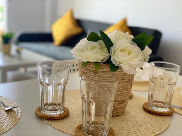 A dining table with a woven basket containing white flowers, two clear glasses, and a woven placemat.