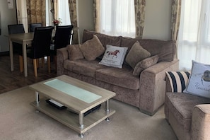A living room with a sofa, a coffee table, a dining table with chairs, and a kitchen area.