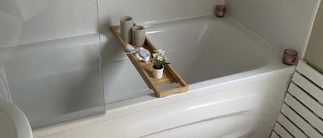 A bathroom with a bathtub, a wooden shelf with toiletries, and a small potted plant.