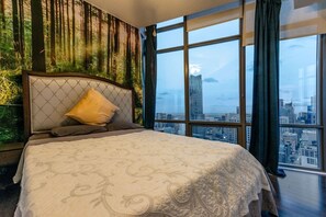 A bedroom with a large bed, a city view through large windows, and a forest-themed wall mural.