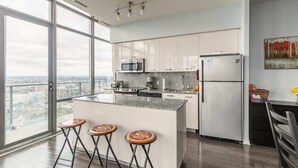 A modern kitchen with a large island, bar stools, stainless steel appliances, and a view of the city. - Spacious 3 Bedroom with stunning city view (Toronto)