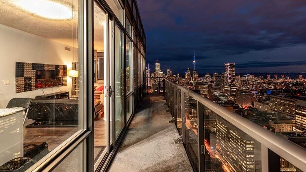 A high-rise building with a balcony overlooking a cityscape at night. - Spacious 3 Bedroom with stunning city view (Toronto)