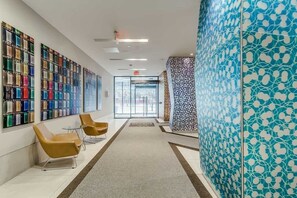 Moderni hotellin aula, jossa on pitkä vastaanottotiski, oleskelualue ja värikkäistä lasitiilistä tehty seinä.