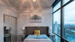 A modern bedroom with a large window, a tufted headboard, and a city view. - Spacious 3 Bedroom with stunning city view (Toronto)