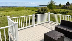 Una terrazza con ringhiere bianche, mobili in vimini e vista su un prato e sull'acqua.