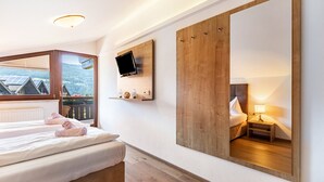 Ein Schlafzimmer mit einem Bett, einem an der Wand montierten Fernseher, einem großen Spiegel und einem Fenster mit Blick auf Gebäude und Grünflächen.