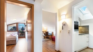 Eine moderne Wohnung mit Holzboden, einer Küche mit weißen Schränken, einem Essbereich mit Tisch und Stühlen sowie einem Schlafzimmer mit Bett und Fenster.