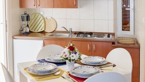 A modern kitchen with white cabinets, a stainless steel range hood, and a dining area with white chairs and a table set for four. - A1 - apt w terrace, just 3 min walk to the beach (Okrug Donji)