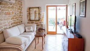 A living room with a stone wall, a sofa, a TV, and a balcony with outdoor furniture. - A1 - apt w terrace, just 3 min walk to the beach (Okrug Donji)
