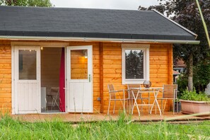 Una cabaña de madera con un porche, una mesa y sillas, y una cortina roja.