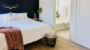 Un dormitorio con una cama, ventilador de techo, pared oscura, una planta y un acceso a un baño.