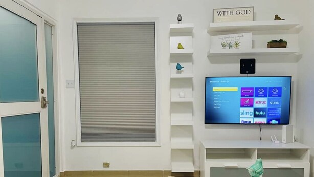 A modern living room with a TV, white shelving, and a decorative vase. - Hollywood Apartments (Yabucoa)